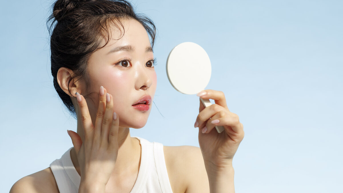 손거울을 들고 볼에 손을 댄 채 얼굴을 살피는 여성